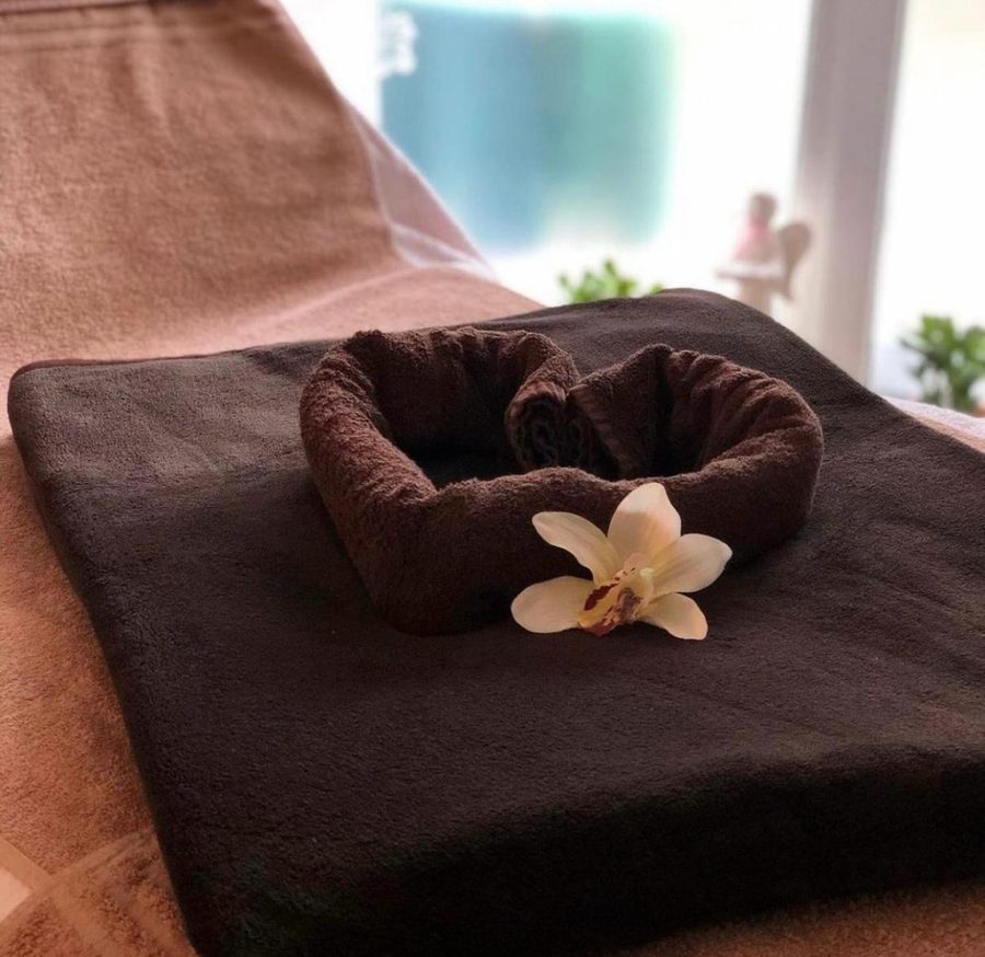 Behandlungsliege mit zu einem Herz gelegtem Handtuch und Orchideenblüte